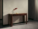The Vao Consoel Table in dark walnut with paneled drawers and tapered legs, styled with a faceted glass vase holding a red flowering branch and a small ivory dish, against a plaster wall.
