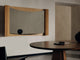 The Aira mirror with a curved and light oak frame mounted above the Bank Oval Dining Table in walnut, with a black sphere on the mirror's ledge and a glass tray on the table.