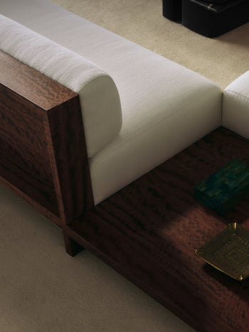 Close-up of Brasa sectional sofa corner in cream bouclé upholstery with a dark walnut wood frame, showing a malachite box and a brass sculptural object resting on the wood base.