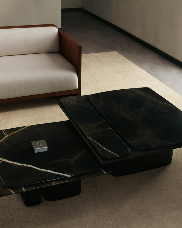 Nested Brio Coffee Tables showcasing the dark stone coffee table corner with veined black-and-gold marble and a brass edge inlay, next to the Brasa Sectional.